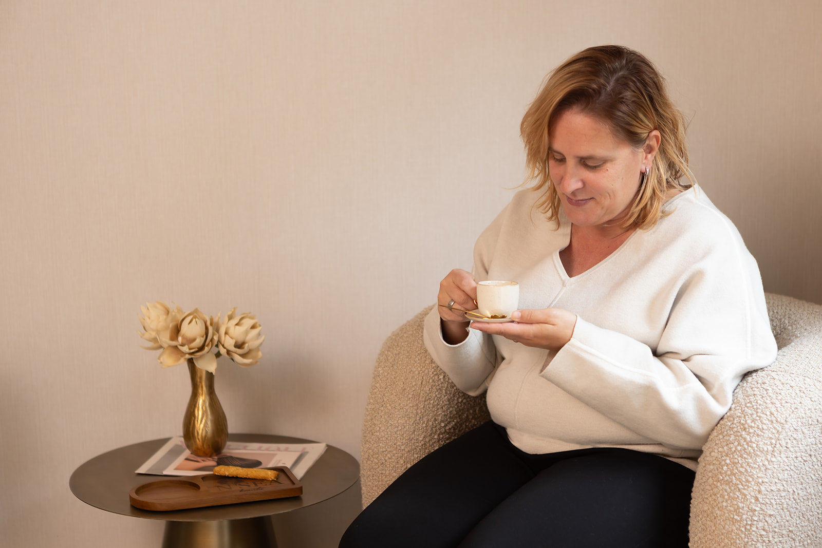 Vrouw ontspant met een kopje koffie in de stijlvolle loungehoek van NSea Beauty. Een plek waar rust en aandacht samenkomen. 