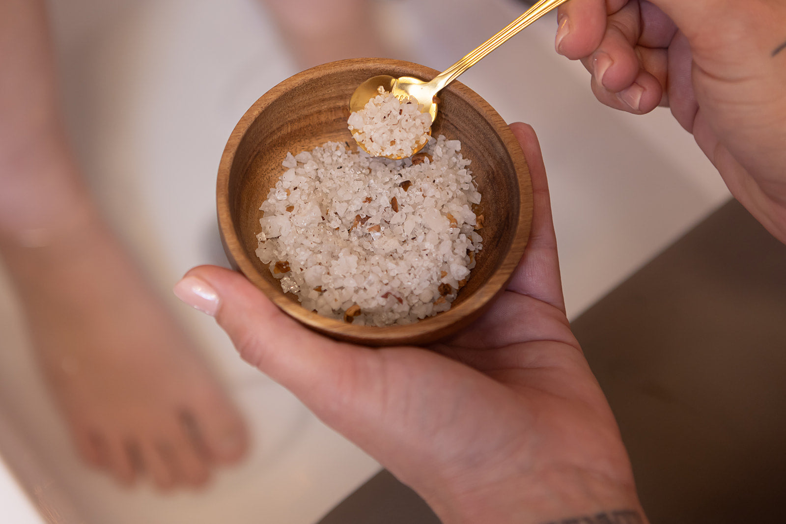 Hand houdt een kom met grove zoutkristallen en kruiden vast - symbool voor het natuurlijke en ontspannende voetritueel bij NSea Beauty, gericht op zuivering en welzijn.