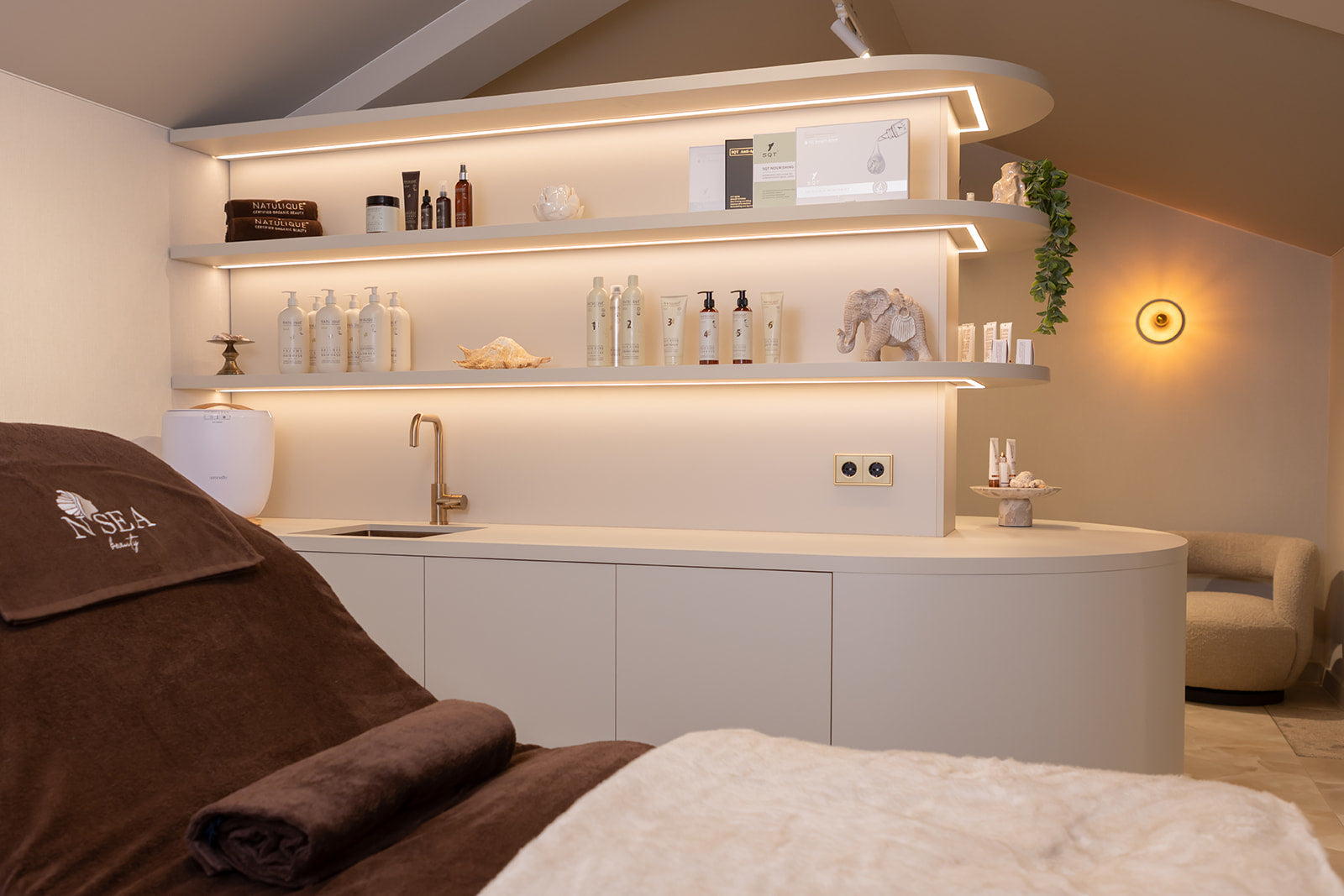 Sfeervolle salonruimte met zachte verlichting en natuurlijke verzorgingsproducten - de kern van holistische huidverbetering bij NSea Beauty.