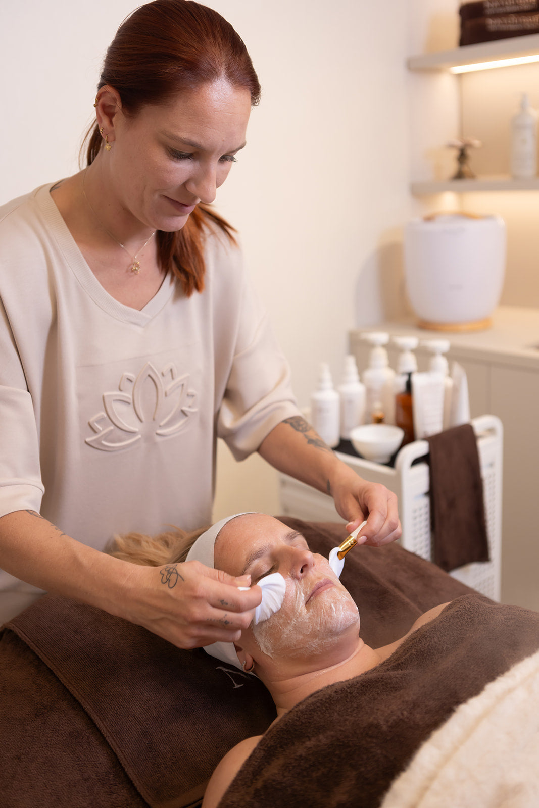 Huidexpert voert een natuurlijke gezichtsbehandeling uit in een rustgevende salonsfeer, omringd door verzorgingsproducten.